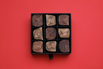 Box of tasty chocolate candies on red background, top view