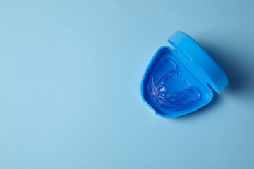 Transparent dental mouth guard in container on light blue background, top view with space for text. Bite correction