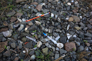 Disposable syringes with needles on heap of stones outdoors