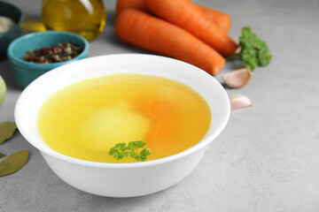 Delicious chicken bouillon and ingredients on light grey textured table, closeup