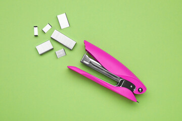 New bright stapler with staples on green background, fat lay. School stationery