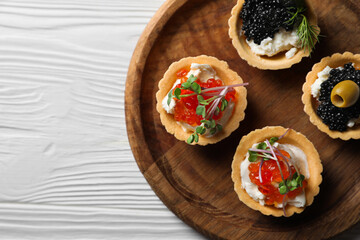 Delicious tartlets with red and black caviar served on white wooden table, top view. Space for text