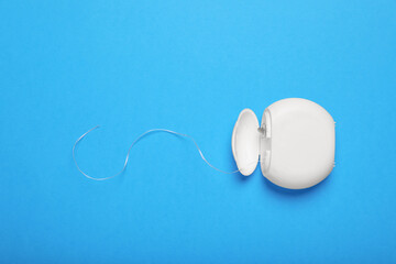 Container with dental floss on light blue background, top view