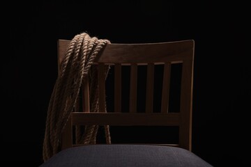 Hostage concept. Wooden chair and rope on dark background