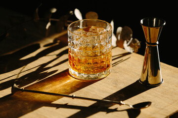 whiskey drink on a wooden table with a barspoon and a jigger 