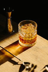 whisky drink on a wooden table with a barspoon and a jigger on black background