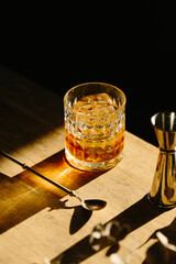 whisky drink on a wooden table with a barspoon and a jigger on black background