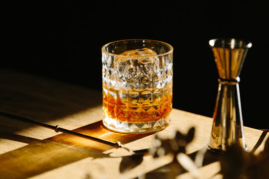 whiskey drink on a wooden table with a barspoon and a jigger on black background