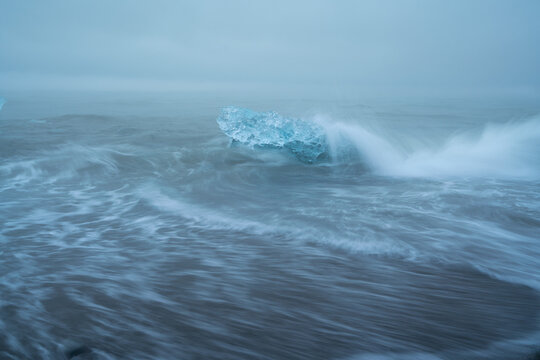 Block of ice being hit by a wave at J&ouml;kuls&aacute;rl&oacute;n beach, Iceland.