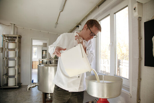 A worker pours fresh milk into a machine in a cheese factory