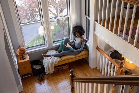 African American Girl relaxing at home reading book in cozy nook 