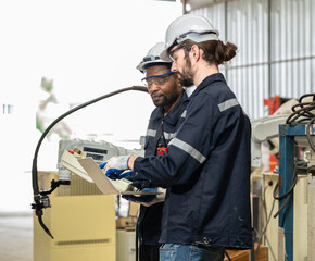 Industrial engineer checking robotic welder operation in modern automation factory. Diverse ethnic...
