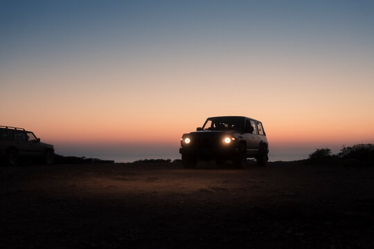 4x4 jeep with headlights on at cliff during sunset