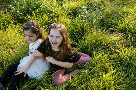 Two sisters sitting outdoors in a field of grass and laughing together