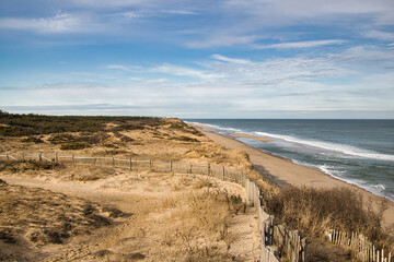 Under a partly cloudy blue sky on a snowless Winter day, the view of the ocean, beach and sand dunes at Marconi Beach, near Wellfleet, MA, on Cape Cod,