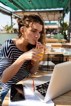 Woman drinking juice watching laptop at terrace bar