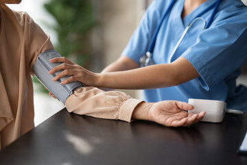 Young woman doctor with stethoscope checking mature patient blood pressure in hospital..