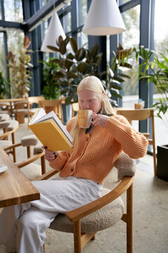 Woman Drinking Cup Of Latte And Reading Book