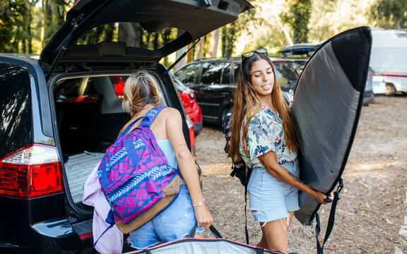 Female surfers taking belongings from car trunk
