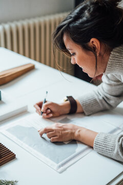 Cropped Image of Woman Writing Project Title on Desk 