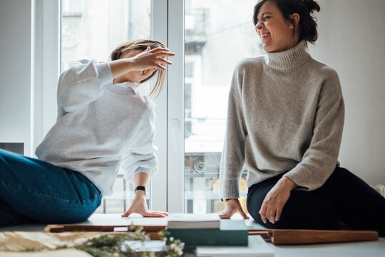 Two Women Sitting on Office Table and Laughing