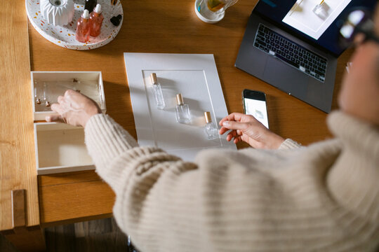 Woman preparing set to photograph perfume at desk