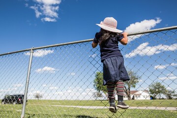 Girl in floppy hat climbing fence