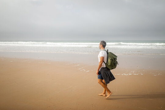young man with backpack walking on the beach