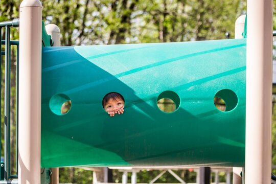 Girl looking through third hole in playground climbing structure