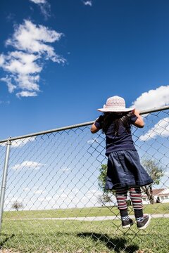 Girl in floppy hat climbing fence