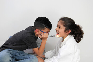 Latino girl and boy play to be a doctor with a white coat that is too big for her and patient who...