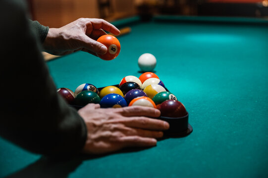 Crop man arranging balls in rack on billiard table