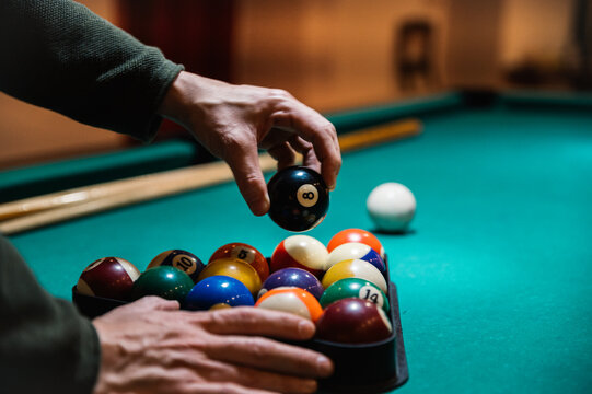 Crop man arranging balls in rack on billiard table