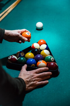 Crop man arranging balls in rack on billiard table