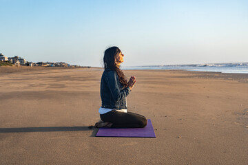Fototapeta premium Side view of a woman sitting on the sand while meditating at sunrise