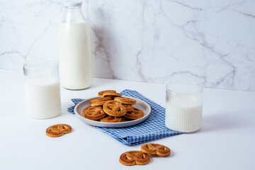 Milk in a glass and a glass bottle on a white table, cookies in