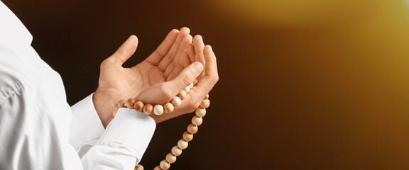 Young Muslim man with prayer beads on dark background, closeup