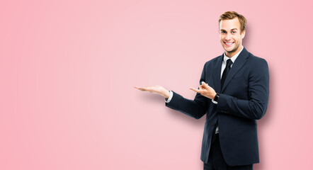 Businessman in black suit showing giving advertising something, isolated on rose pink background....