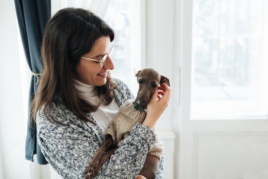 Portrait of a woman holding mini greyhound in her arms.