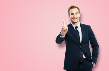 Excited businessman in black confident suit showing two fingers or victory sign gesture, over pink...