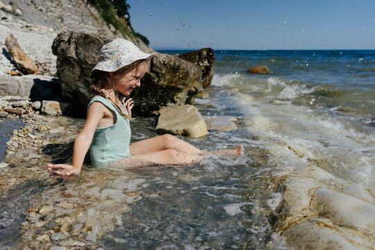 Female Kid Playing In Water On Rocky Beach