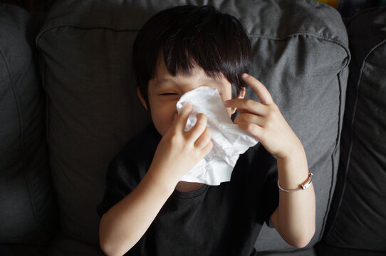 Cute little asian boy is wiping his nose while laughing