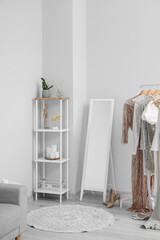 Interior of light makeup room with clothes, mirror and shelving unit