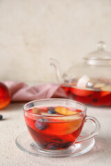 Glass cup of fruit tea with blueberries, apple and peach on light background, closeup