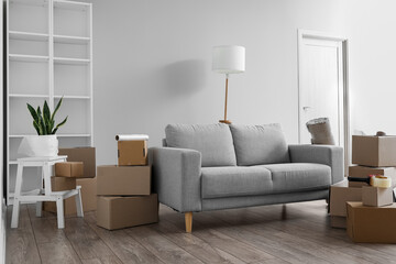 Cardboard boxes with grey sofa, stepladder and lamp in living room on moving day