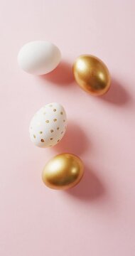 Vertical video of white and gold easter eggs on pink background
