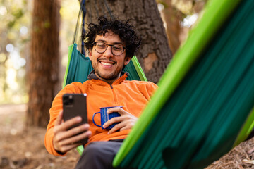 Outdoorsy Man Uses Phone While Resting In A Hammock In Nature