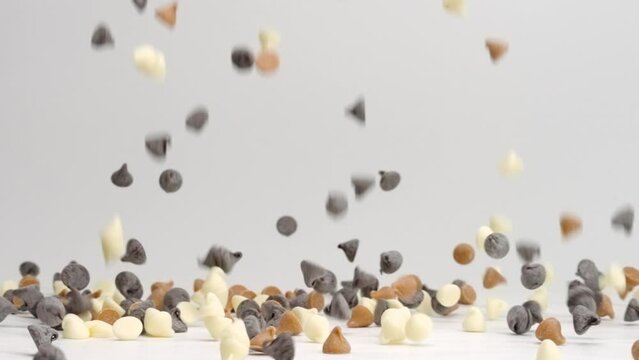 Milk semi sweet, butterscotch caramel and white chocolate chips falling and bouncing on white table top in slow motion