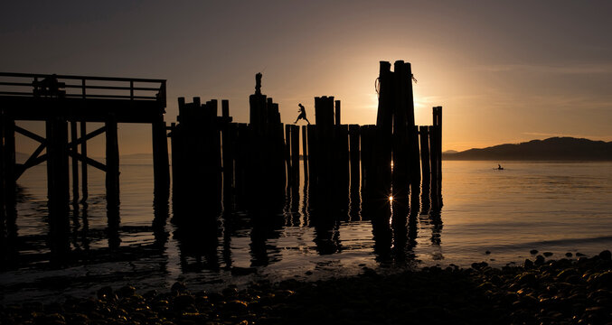 Wooden post on shore against sky during sunset