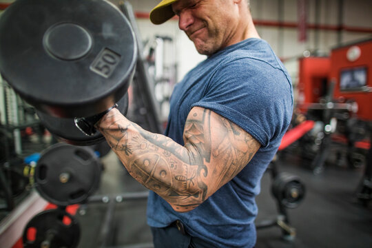 Cropped view of man training biceps in gym with dumbbells